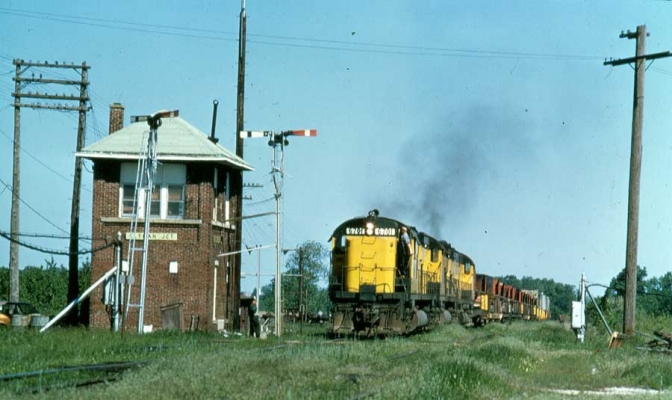Tower  Clyman Junction, WI
The interlocking tower at Clyman Junction, WI governed the diamond for the East/West Adams Sub and North/South Janesville Sub.  An eastbound train with Alco C628 #6701 is picking up train orders.  Chuck Porter photo.  Submitted by J. H. Yanke
Keywords: Tower Clyman Junction 6701